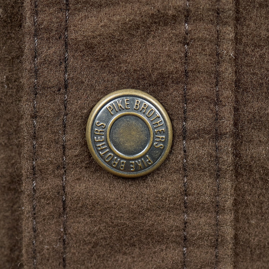 A close-up of a circular bronze button on a brown textured fabric, featuring the embossed brand name 'PIKE BROTHERS'.