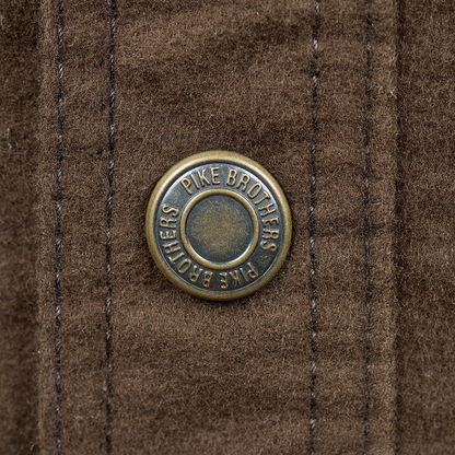 A close-up of a circular bronze button on a brown textured fabric, featuring the embossed brand name 'PIKE BROTHERS'.