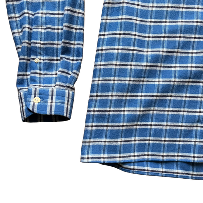Close-up of a blue plaid flannel shirt showing the sleeve cuff with two buttons and a detailed view of the fabric pattern 
