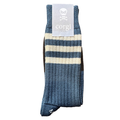A single ribbed knit sock in blue and cream stripes, with a light gray paper tag attached at the top featuring a skull logo and the word 'corgi'.