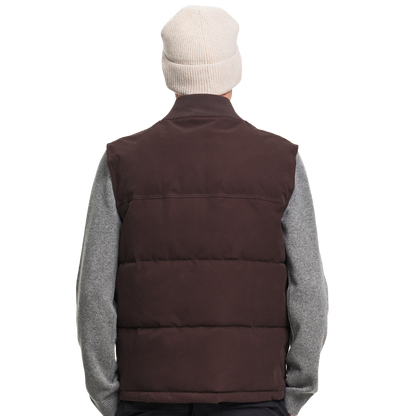 A person shown from the back wearing a dark brown puffer vest over a heather gray long-sleeve shirt, with a cream knit beanie on a plain white background.