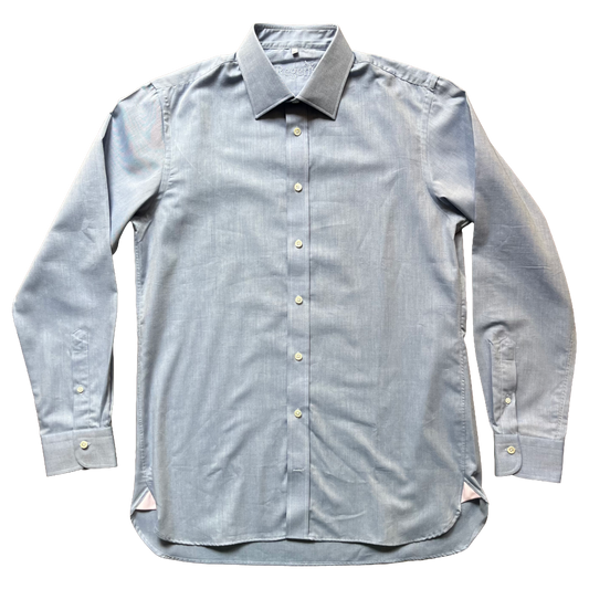 A light blue chambray long-sleeve button-down shirt with a pointed collar and light-colored buttons, laid flat against a white background.