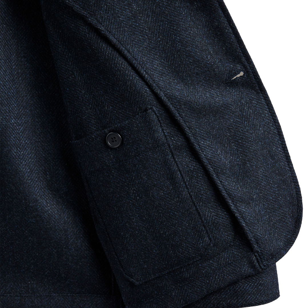 Close-up detail of a dark navy textured fabric jacket, showing a pocket with a button and the woven texture of the material.