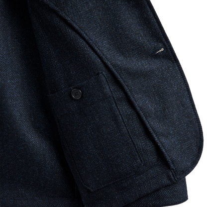 Close-up detail of a dark navy textured fabric jacket, showing a pocket with a button and the woven texture of the material.