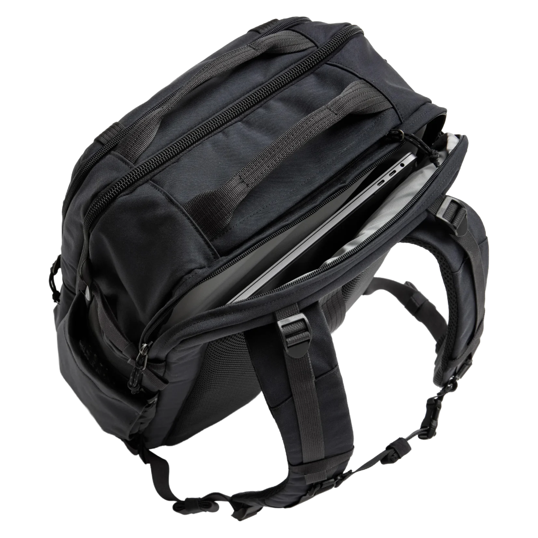 A black tactical backpack shown from an angled top view, with its main compartment open to reveal a silver laptop inside. The backpack features multiple zippered compartments, padded shoulder straps, and a structured, durable design, photographed against a solid white background.
