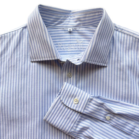A close-up of a light blue and white striped dress shirt with a pointed collar, button placket, and folded cuff, shown on a white background.