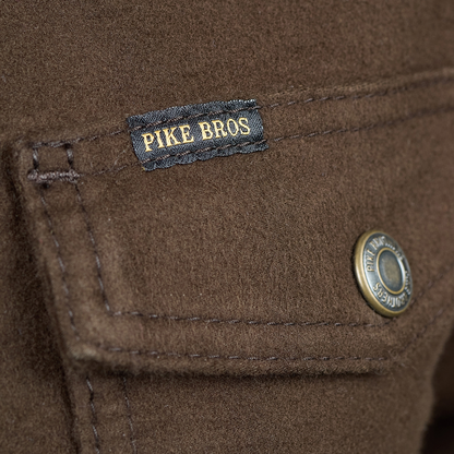 Close-up of a brown wool jacket showing a black 'PIKE BROS' brand label with gold embroidery and a brass snap button.