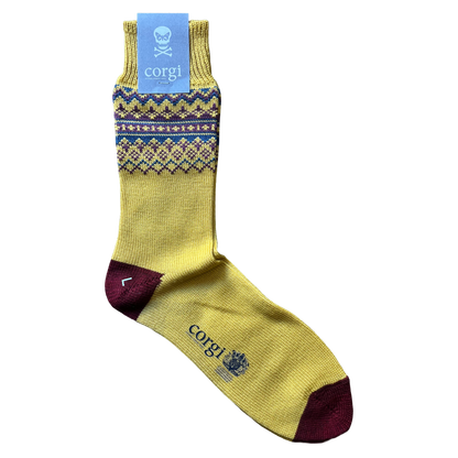A single yellow crew sock with a blue and purple Fair Isle pattern band, a dark burgundy heel, and a dark burgundy toe. The sock features the brand name 'corgi' printed in blue near the foot, and is shown with its light blue paper tag attached against a plain white background.