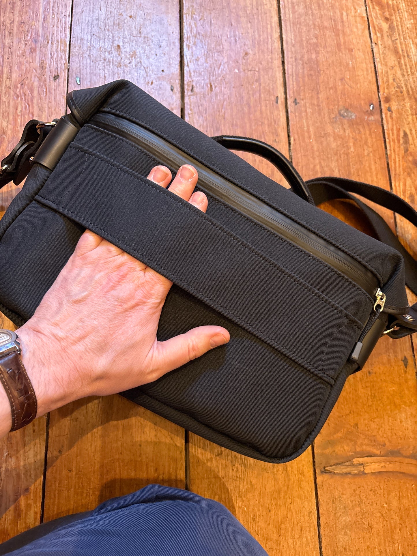 Hand holding a black bag on a wooden floor