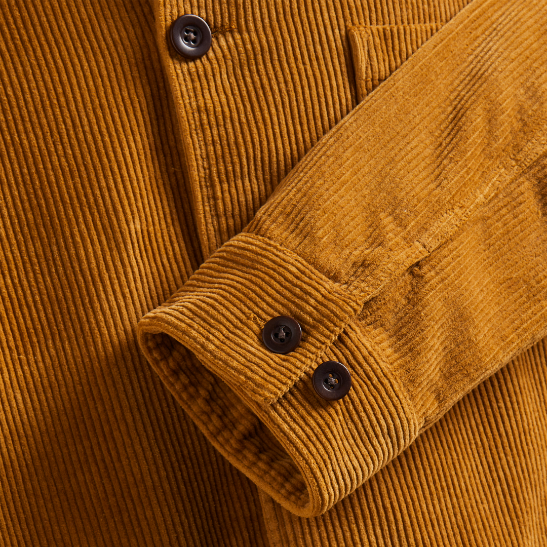 Close-up of a mustard yellow corduroy button-up shirt with a buttoned cuff and dark buttons.