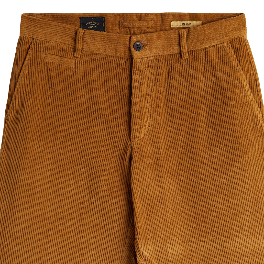 Close-up of a pair of corduroy trousers in a warm camel brown color, showing the waistband, button closure, belt loops, and front pockets.