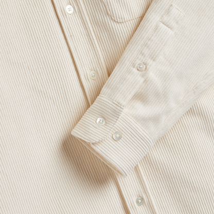 Close-up of a cream-colored ribbed corduroy shirt with matching buttons and a folded cuff.