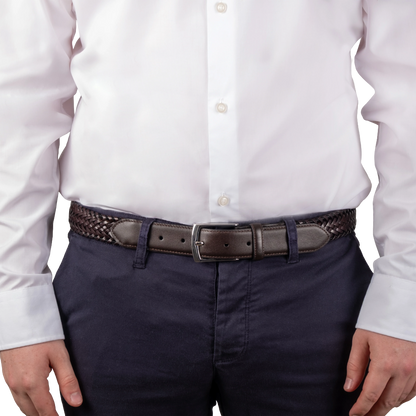 A close-up of a person wearing a dark brown woven belt with a dark brown leather buckle, paired with navy blue trousers and a white button-down shirt.