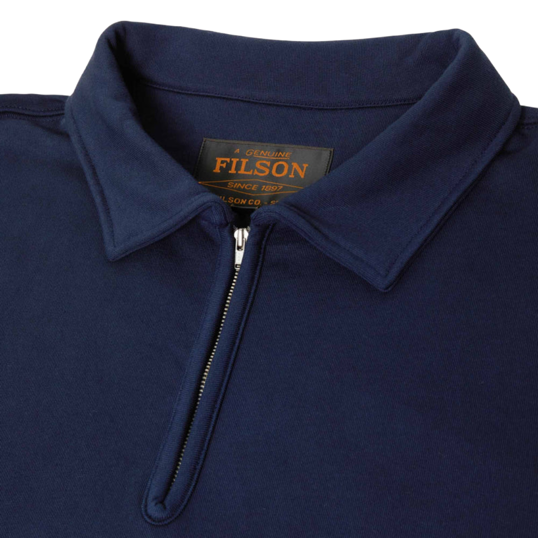 Close-up of a navy blue polo shirt collar with a half-zip neckline, showing the black and gold FILSON neck label.