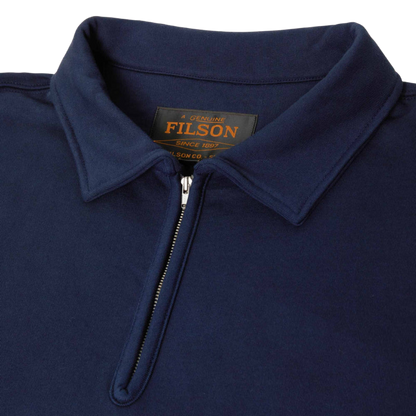 Close-up of a navy blue polo shirt collar with a half-zip neckline, showing the black and gold FILSON neck label.