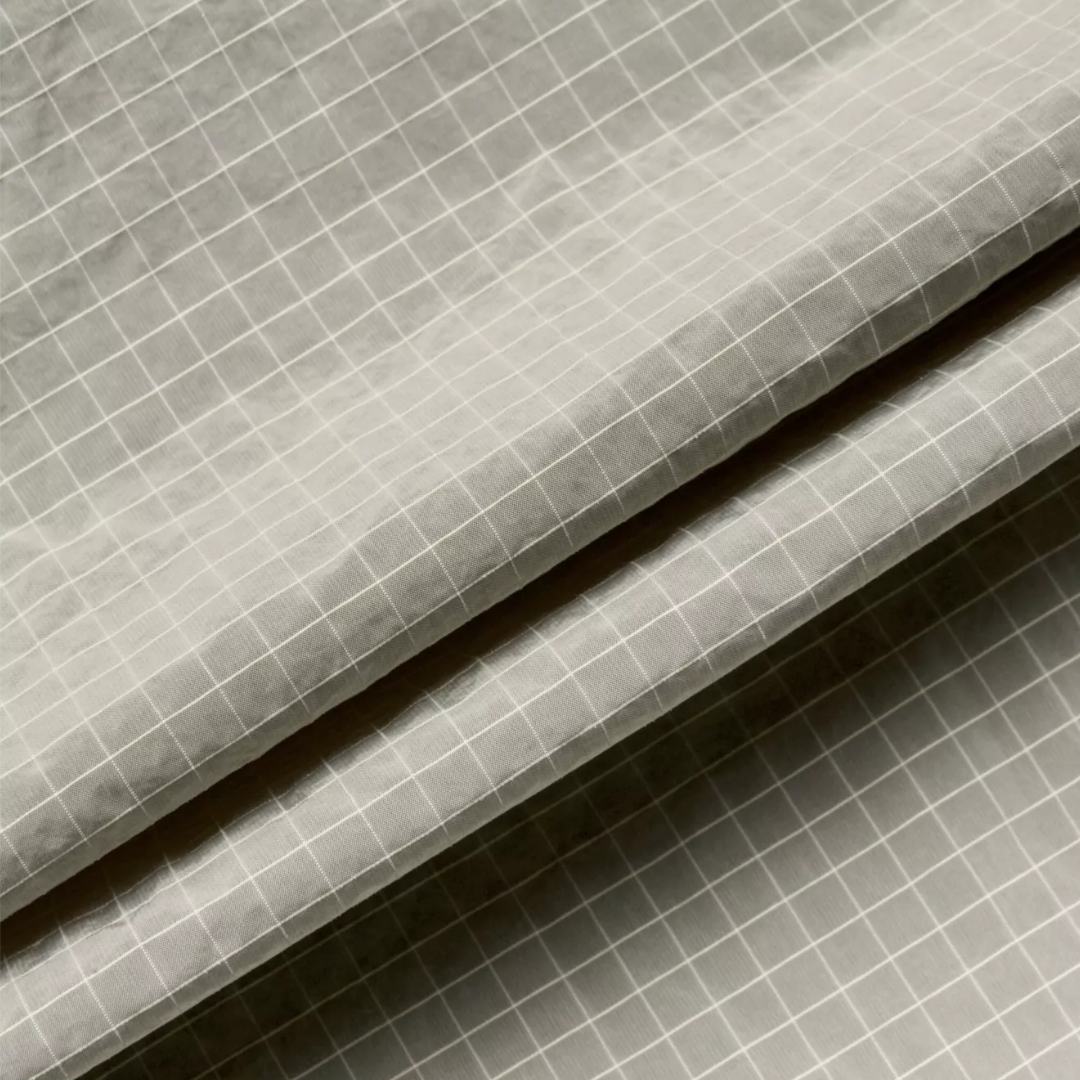 A close-up of draped gray fabric with a fine white grid pattern, showing the texture and folds.