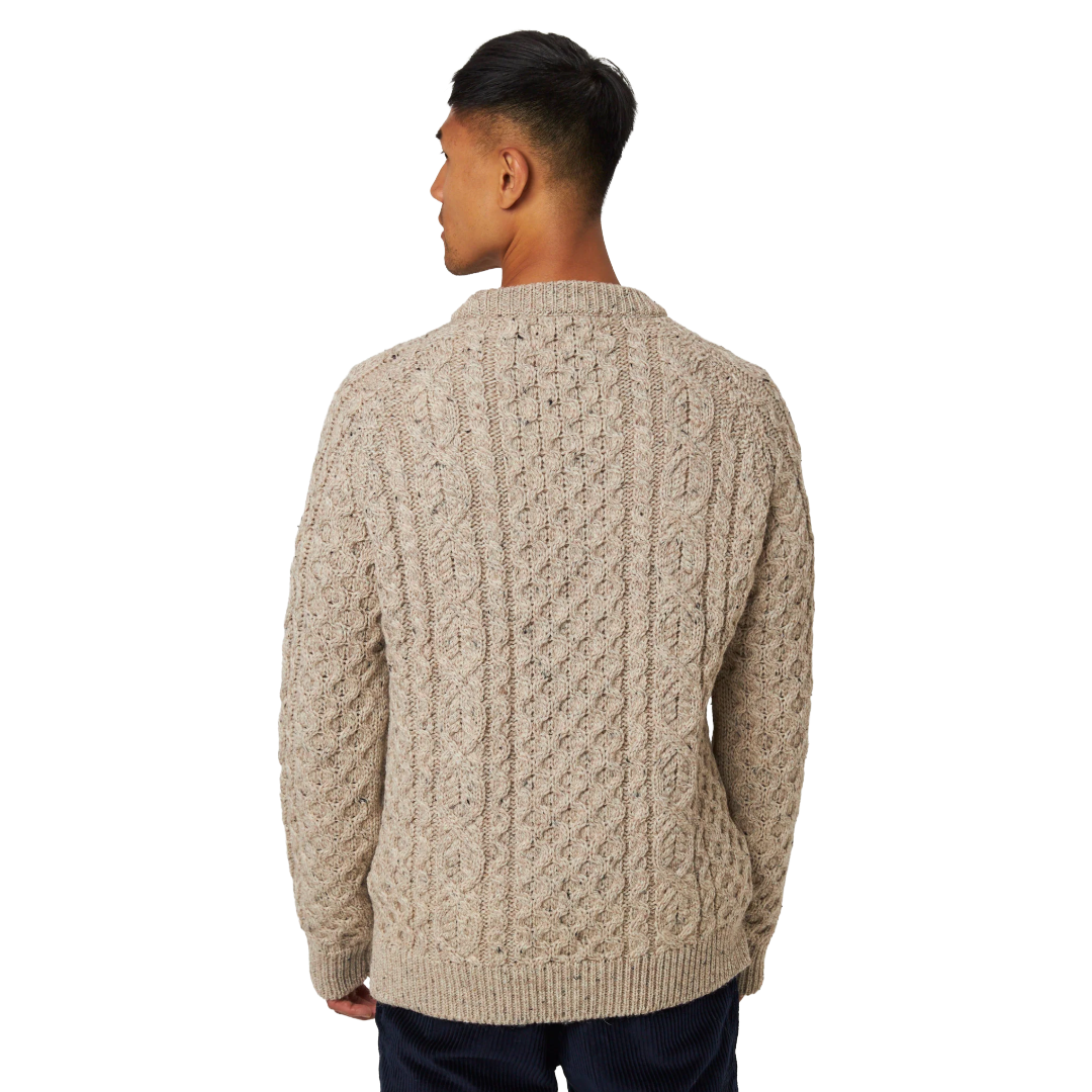 A man viewed from the back wearing a beige cable-knit sweater and dark navy pants, set against a plain white background.