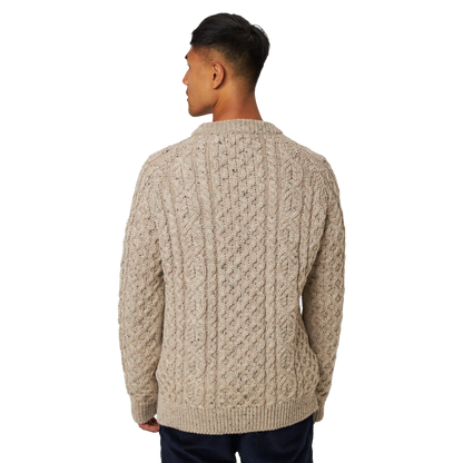 A man viewed from the back wearing a beige cable-knit sweater and dark navy pants, set against a plain white background.