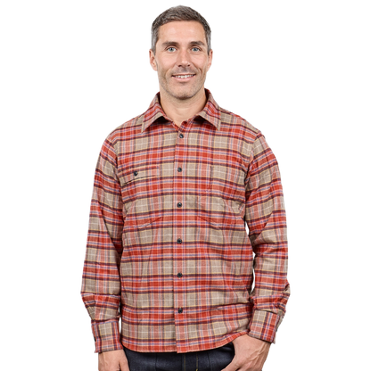 A man wearing a long-sleeve button-up plaid shirt in red, orange, and beige tones, paired with dark jeans, photographed against a solid white background.