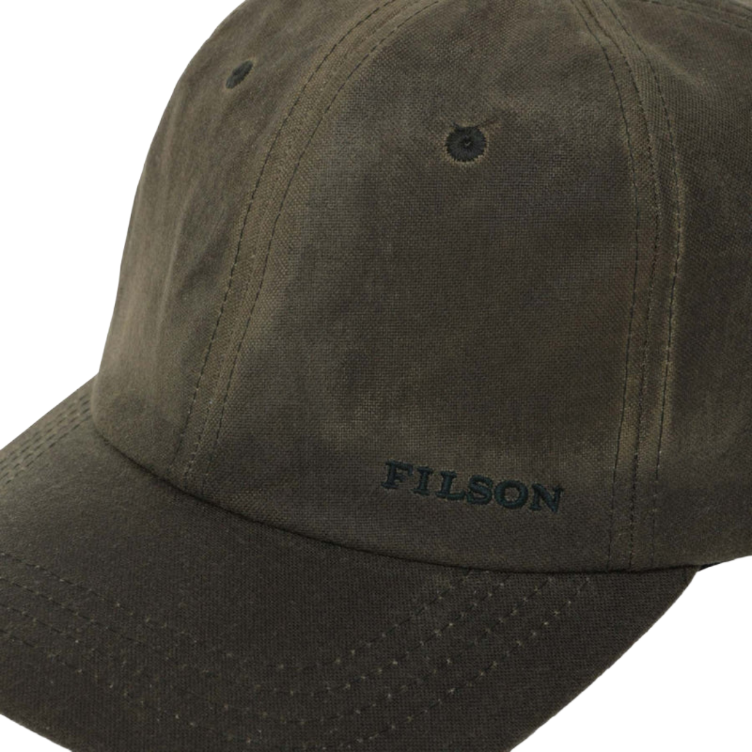 Close-up of a dark olive green Filson baseball cap on a white background, showing the embroidered brand name on the brim.