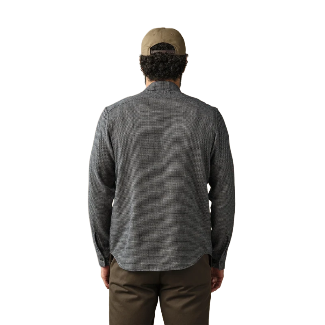 A man viewed from behind wearing a dark gray textured long-sleeve shirt, brown pants, and a tan baseball cap against a plain white background.