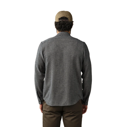 A man viewed from behind wearing a dark gray textured long-sleeve shirt, brown pants, and a tan baseball cap against a plain white background.