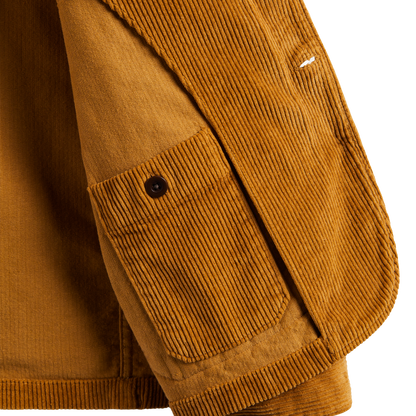 Close-up detail of a mustard brown corduroy jacket showing a buttoned chest pocket and ribbed fabric texture against a white background.