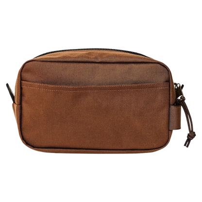 A brown canvas toiletry bag with a top zipper, front slip pocket, and side strap closure, shown against a plain white background.