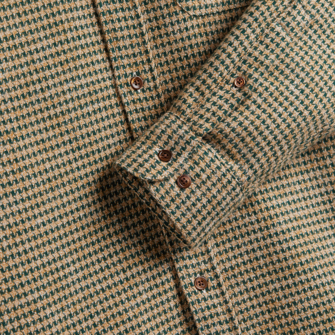 Close-up of a houndstooth patterned button-down shirt in beige and dark green, showing the fabric texture and brown buttons.