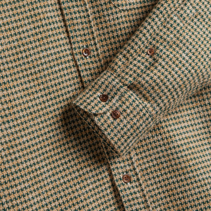 Close-up of a houndstooth patterned button-down shirt in beige and dark green, showing the fabric texture and brown buttons.