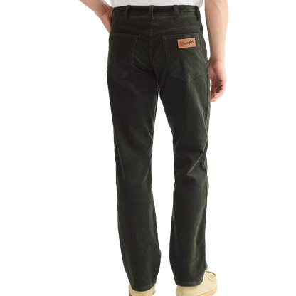 Rear view of a person wearing dark charcoal gray denim jeans with a brown leather Wrangler patch on the back pocket, paired with a white shirt and beige shoes, on a white background.