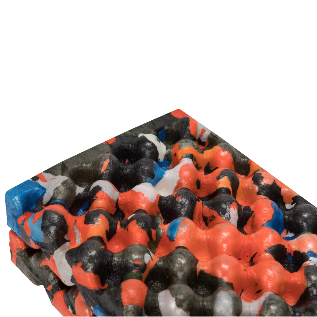 A close-up of a textured, bubbled material sample with a multicolor pattern of bright orange, black, white, and blue on a plain white background.