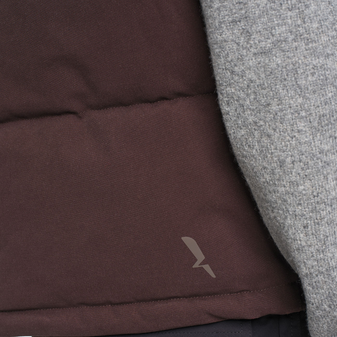 Close-up of a dark brown puffer vest with a small gray logo, layered over a heather gray knit garment.