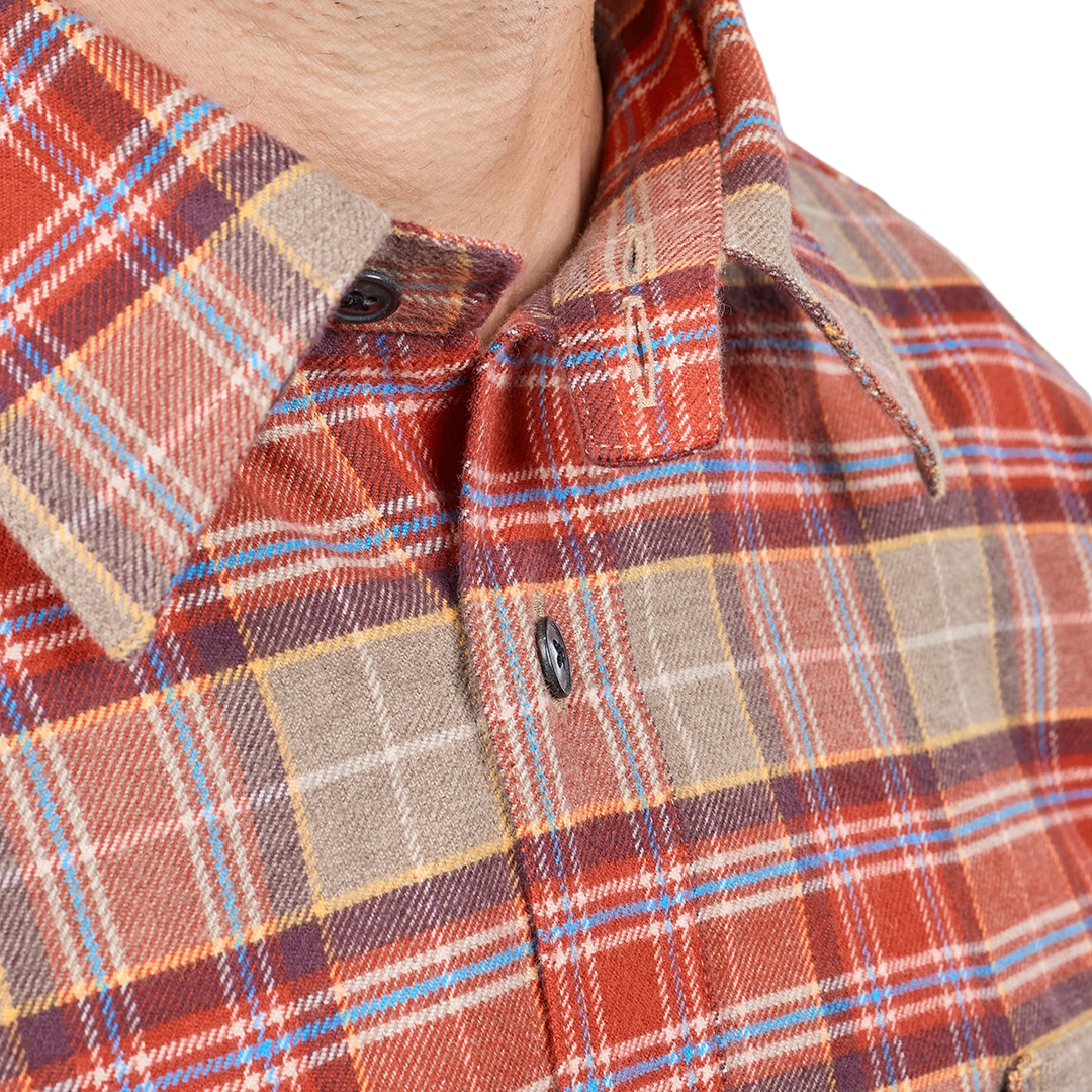 Close-up of a men's long-sleeve plaid button-down shirt on a model, featuring a warm red-orange base with beige, brown, and light blue stripes.