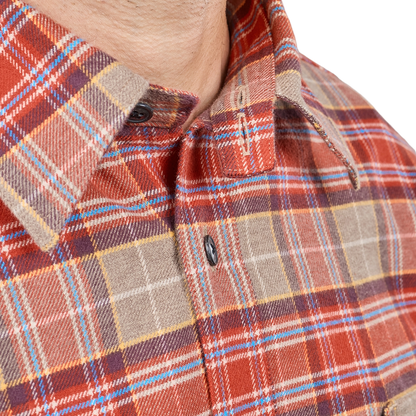 Close-up of a men's long-sleeve plaid button-down shirt on a model, featuring a warm red-orange base with beige, brown, and light blue stripes.