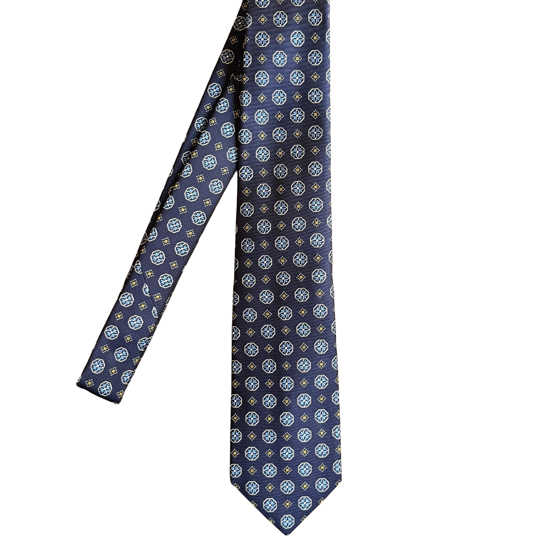 A navy blue necktie with a repeating geometric medallion pattern in white, light blue, and gold, displayed against a solid white background.