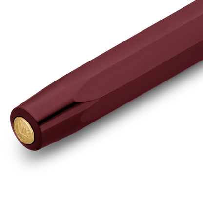 A close-up of a luxury pen featuring a deep burgundy barrel and a polished gold-tone end cap with an embossed logo, set against a clean white background.