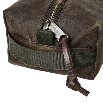 Close-up of a dark olive green waxed canvas pouch with a silver-toned metal zipper, a dark olive green webbing loop, and a brown leather zipper pull tab engraved with the brand name 'FALCON'.
