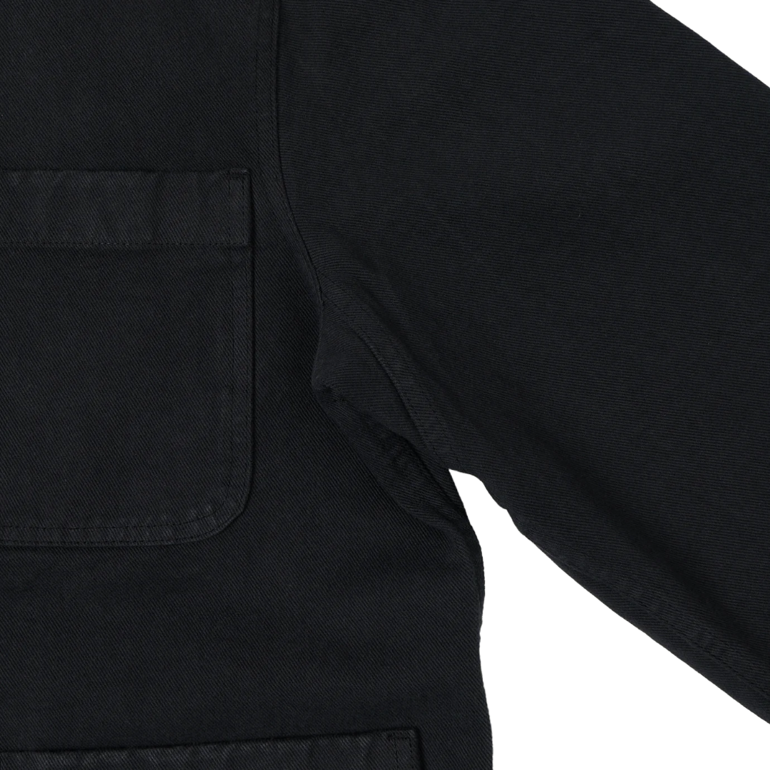 Close-up detail of a black canvas utility jacket showing a chest pocket and sleeve seam against a white background.