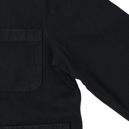Close-up detail of a black canvas utility jacket showing a chest pocket and sleeve seam against a white background.