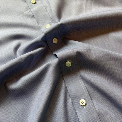 Close-up of a light blue-gray textured button-down shirt with pale yellow buttons, showing the fabric weave and collar construction.