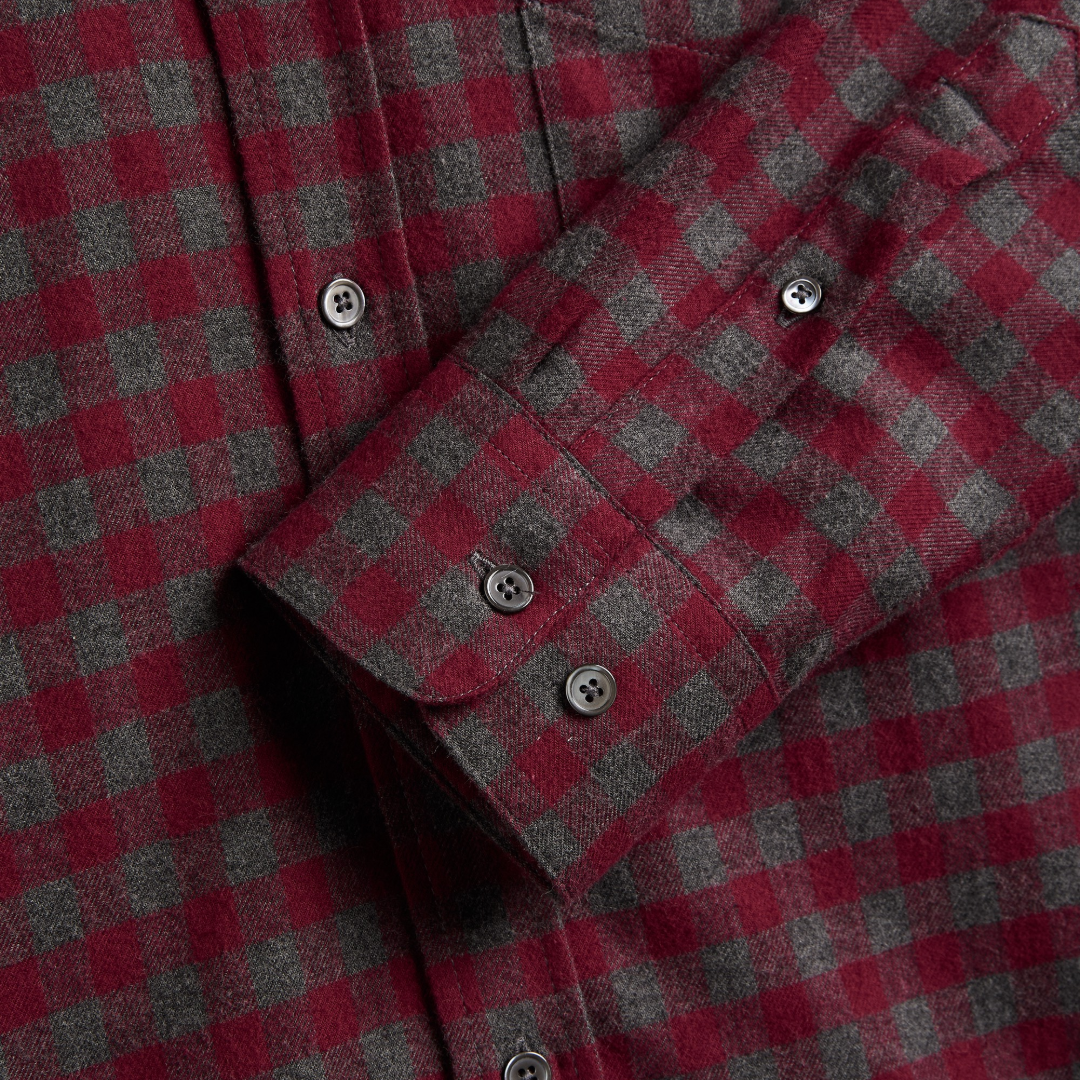 Close-up of a red and gray checkered flannel shirt with silver buttons, showing the fabric texture and cuff detail.