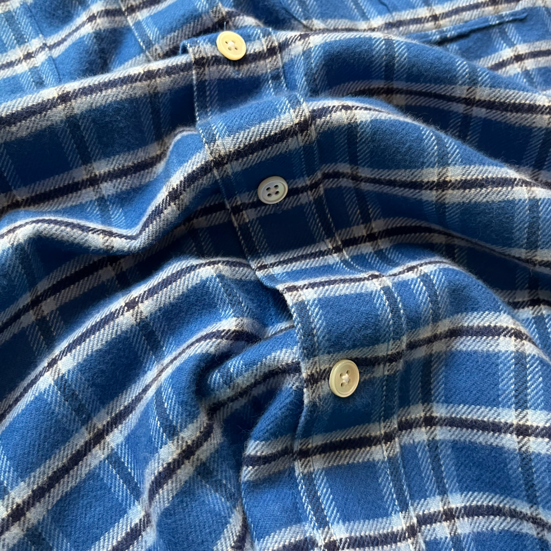 A close-up of a blue check shirt fabric, showing the texture of the woven material, white buttons, and the pattern details.