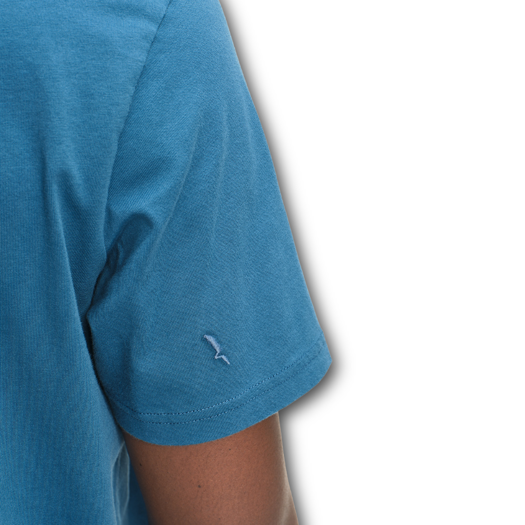 Close-up of the sleeve of a blue Aigle t-shirt with a small logo on a white background sold at Regent in Salisbury