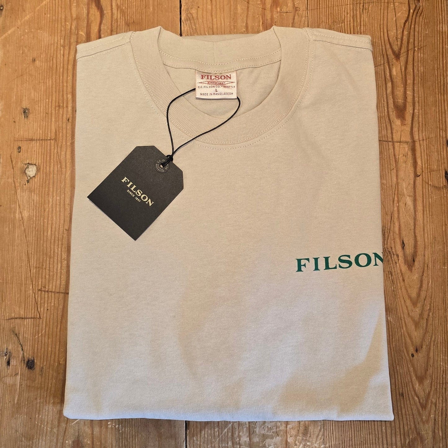 Beige t-shirt with 'Filson' branding on a wooden surface
