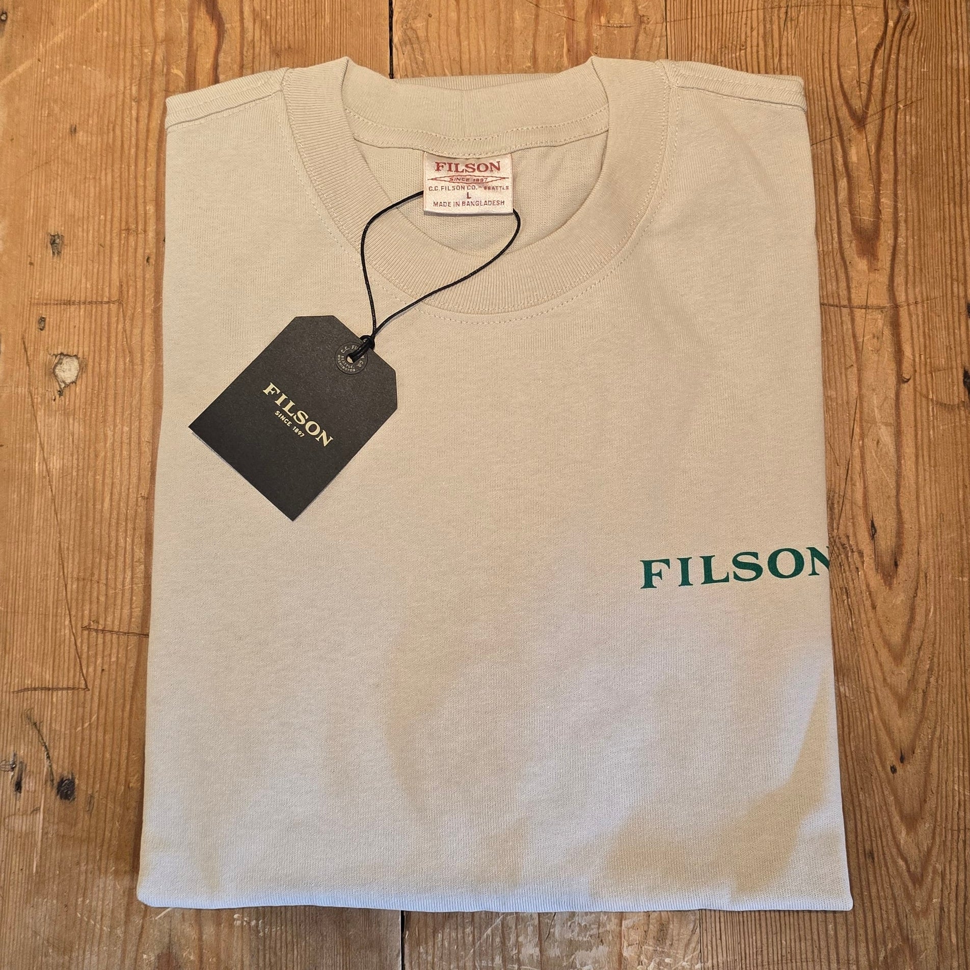 Beige t-shirt with 'Filson' branding on a wooden surface