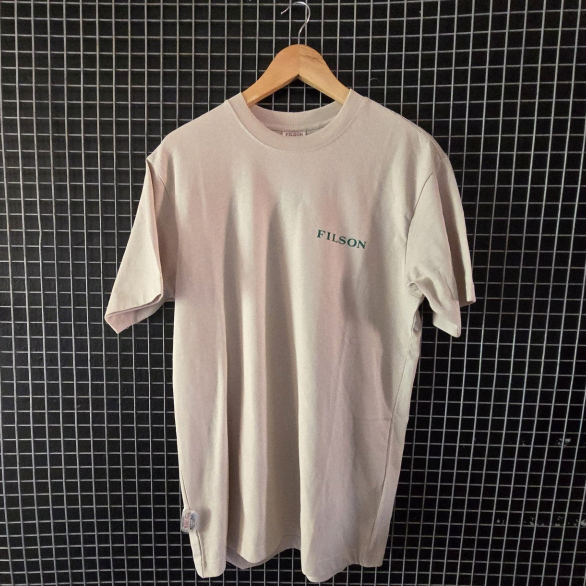 Beige t-shirt with 'Fusion' logo on a hanger against a grid wall.