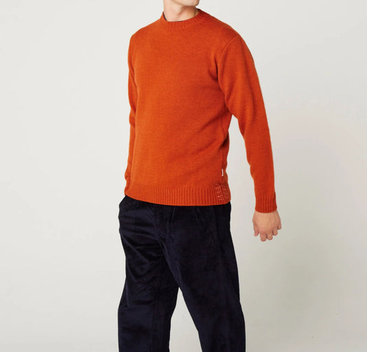 Person wearing an orange sweater and dark pants on a plain background