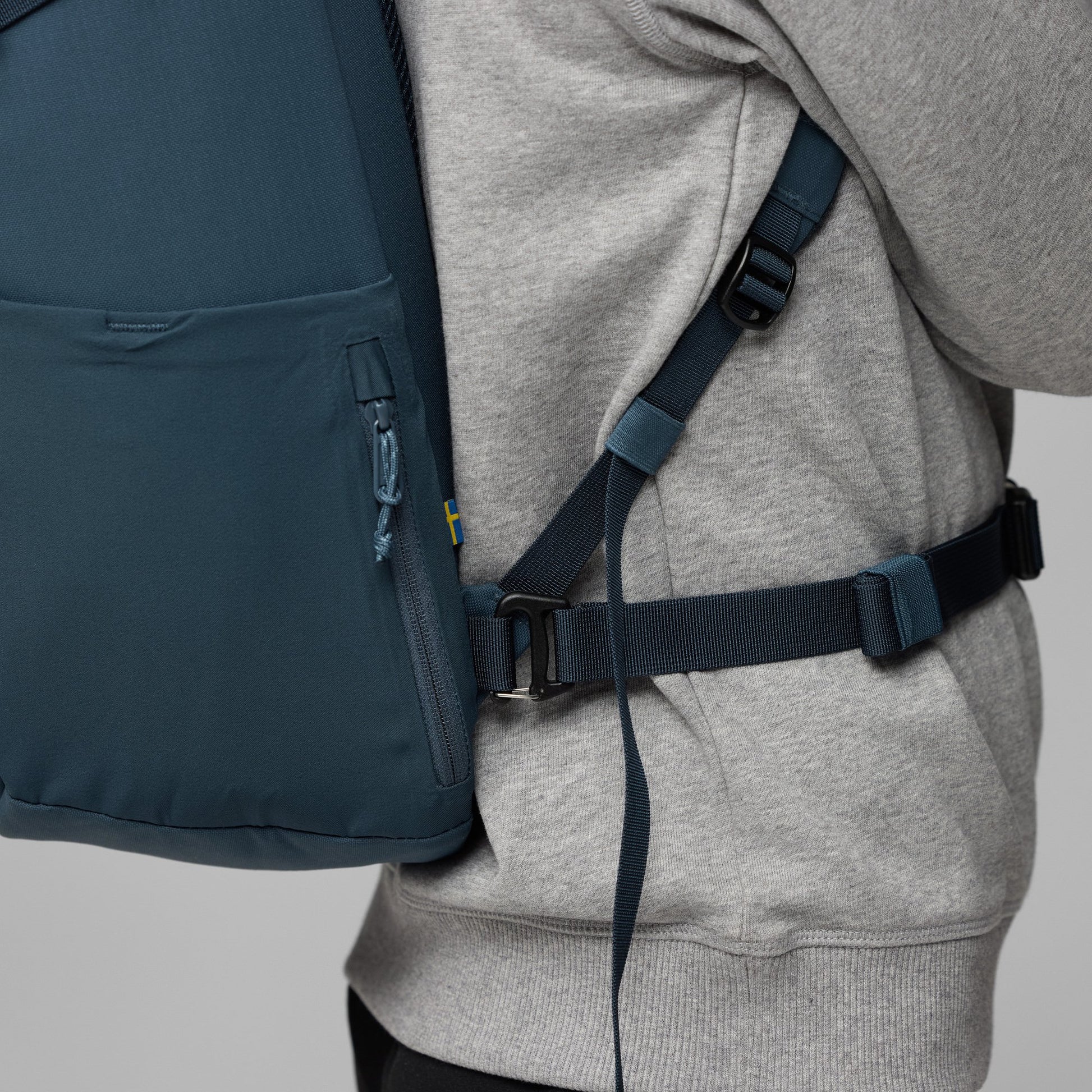 Person wearing a gray hoodie with a navy backpack on a light gray background