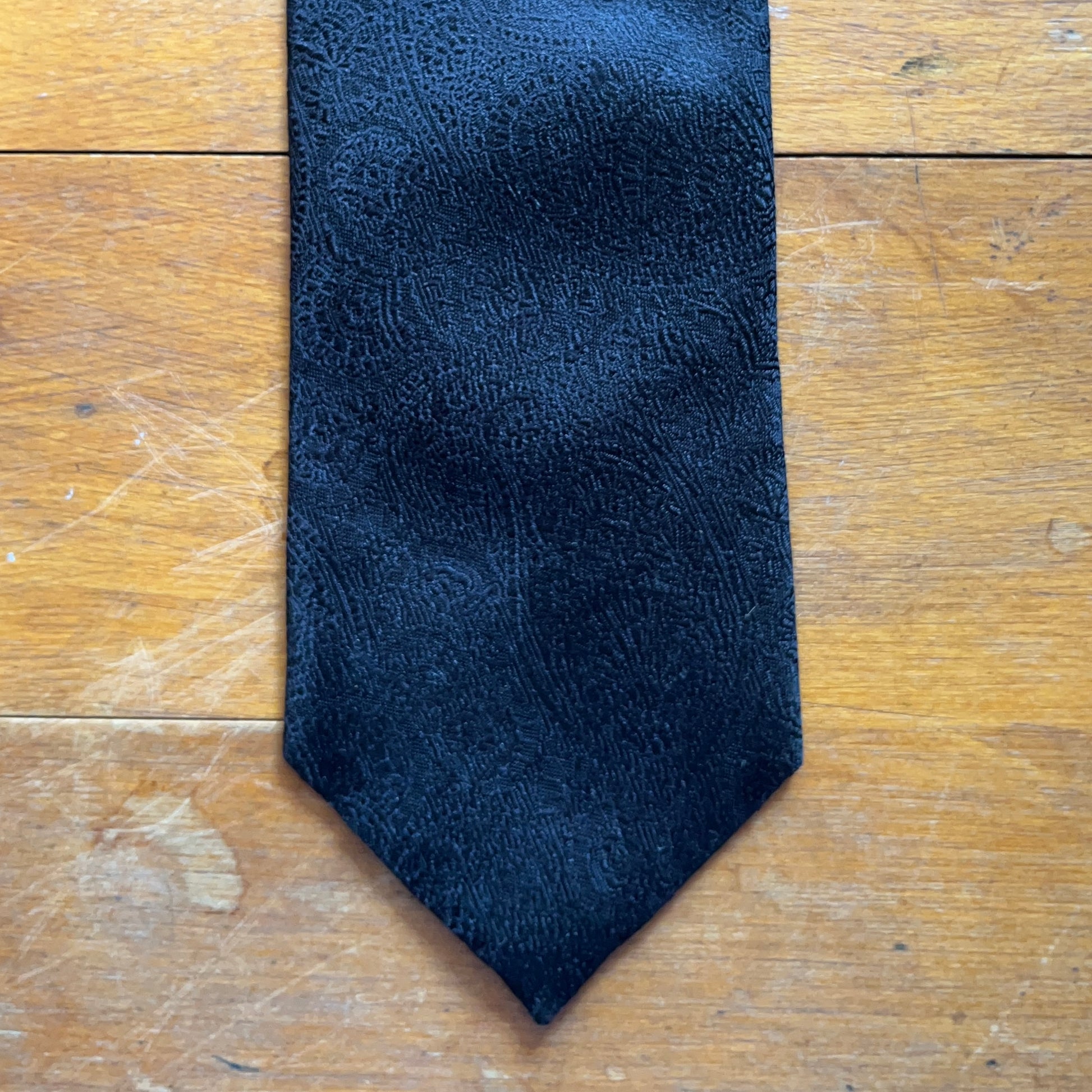 Handmade black silk tie with paisley closeup of blade design set against wooden boards